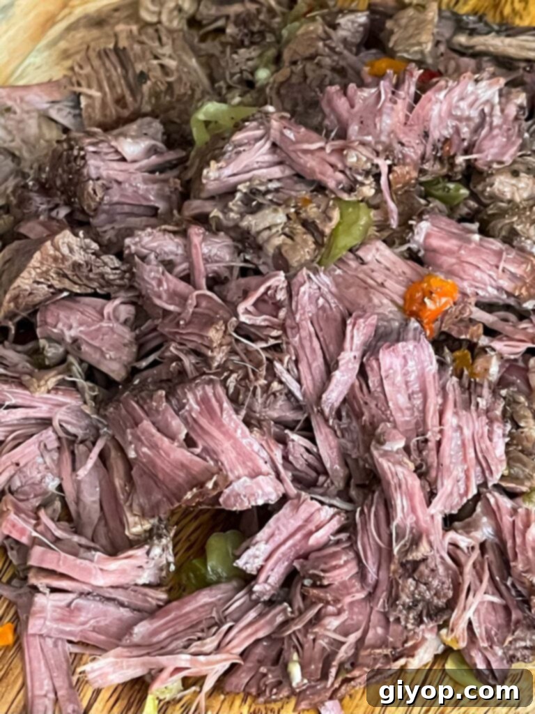 Perfectly shredded Italian beef piled high on a rustic wooden cutting board.