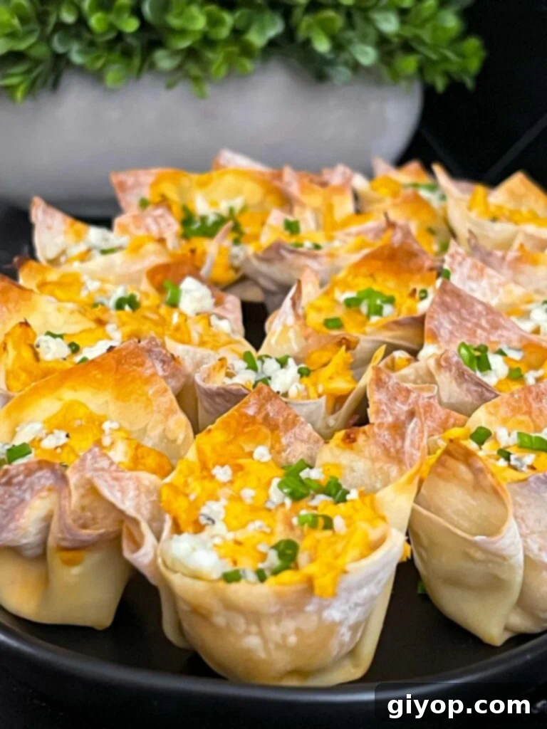 Buffalo chicken wontons garnished with chives and blue cheese crumbles on a cutting board, ready to be served.