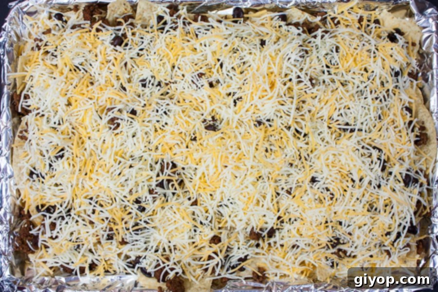Loaded Sheet Pan Beef Nachos 5 Tortilla chips, seasoned ground beef, black beans, and shredded cheese ready for the oven on a foil-lined baking sheet.