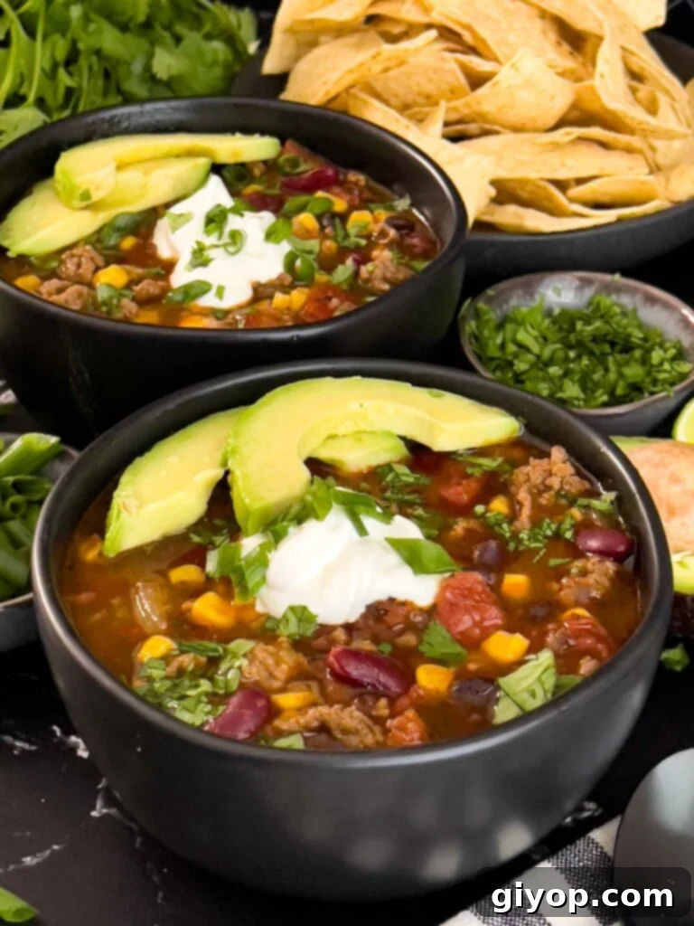 Bowls of taco soup in dark bowls with many garnishes, including sour cream, cilantro, and tortilla chips.