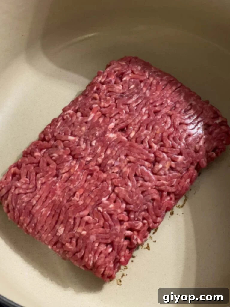 Raw ground beef in a dutch oven, starting to brown.