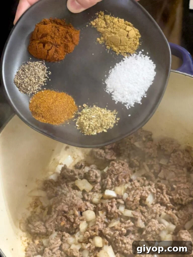 A mix of ground spices being added on top of cooked ground beef and onions.