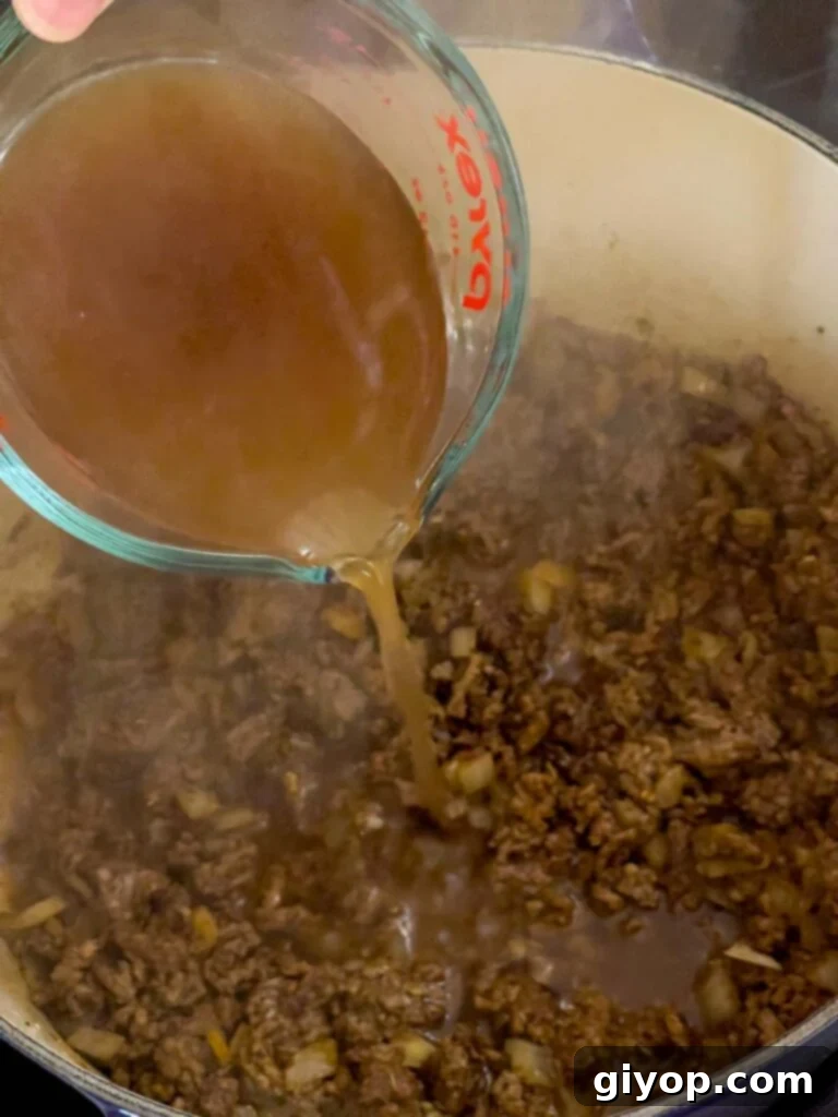 Beef broth being poured into the dutch oven with cooked beef and spices.