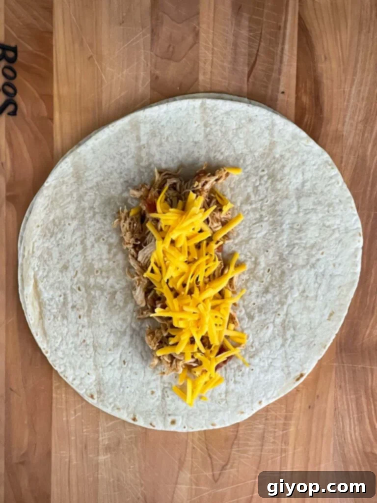 Shredded Mexican chicken and shredded sharp cheddar cheese in the middle of a burrito size tortilla.
