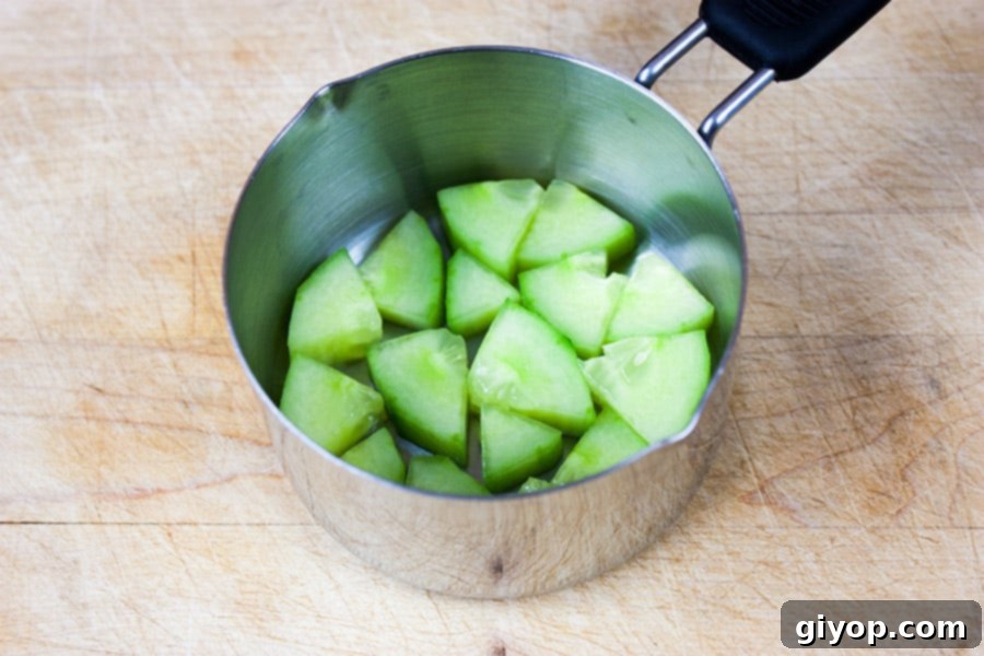 Freshly diced cucumber layered at the bottom of a metal measuring cup, ready for building the sushi stack.