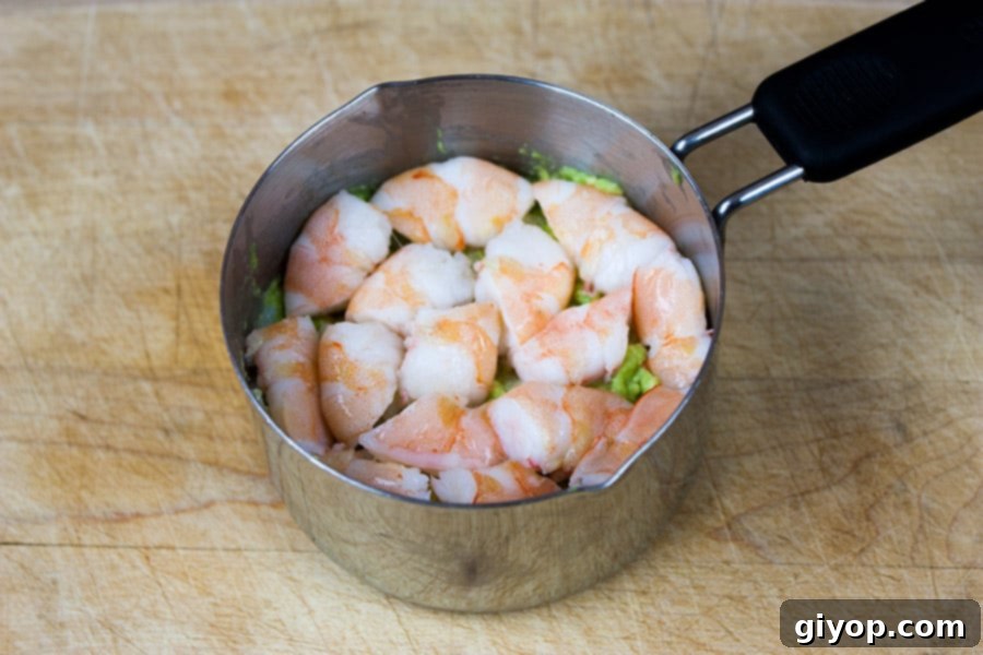 Diced shrimp pieces neatly arranged in a layer within the metal measuring cup, building up the sushi stack.
