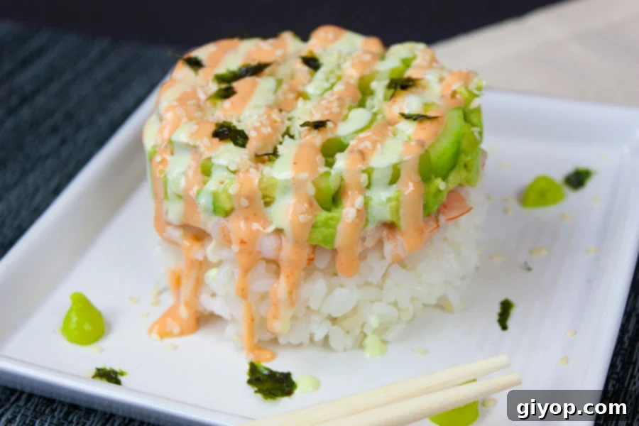 A finished Spicy Shrimp Sushi Stack, generously drizzled with wasabi and sriracha sauces, served with chopsticks on a white square plate.