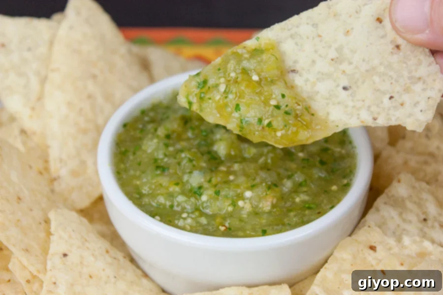 A tortilla chip being dipped into a bowl of vibrant green homemade roasted tomatillo salsa (salsa verde).