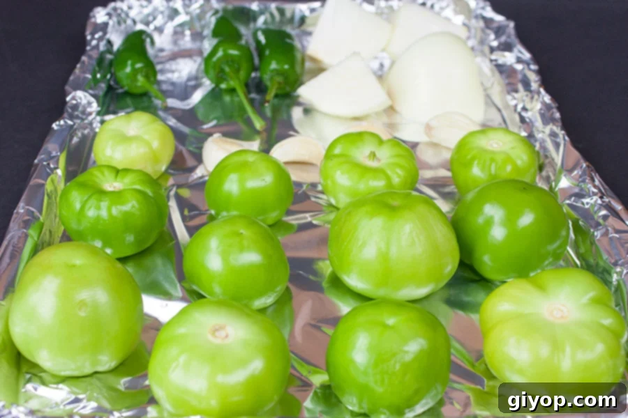 Raw tomatillos, jalapeños, and onions laid out on a foil-lined baking sheet, ready for roasting for homemade roasted tomatillo salsa (salsa verde).