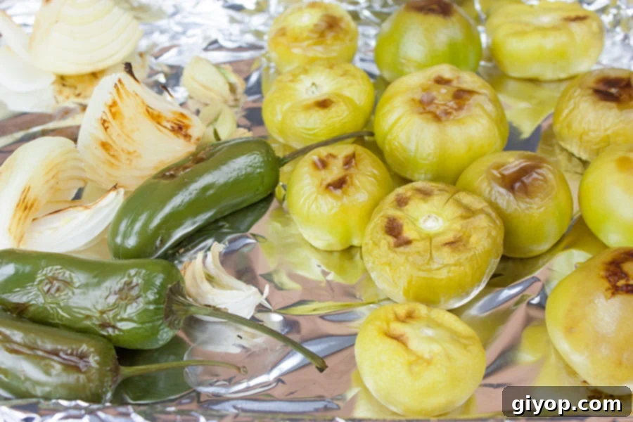Roasted tomatillos, jalapeños, and onions fresh out of the oven, on a foiled lined baking sheet for homemade roasted tomatillo salsa (salsa verde).