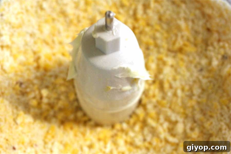 A bowl of a food processor filled with freshly shredded sharp cheddar cheese, ready for mixing. The cheese appears bright orange and finely grated.