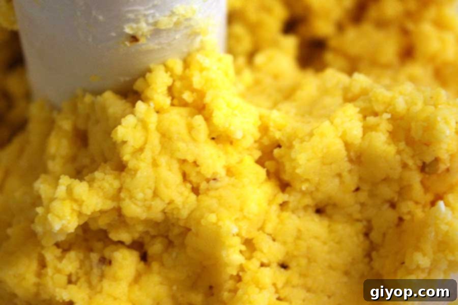 The food processor bowl contains a forming ball of spicy cheese cracker dough, showing its pliable and slightly yellow texture.