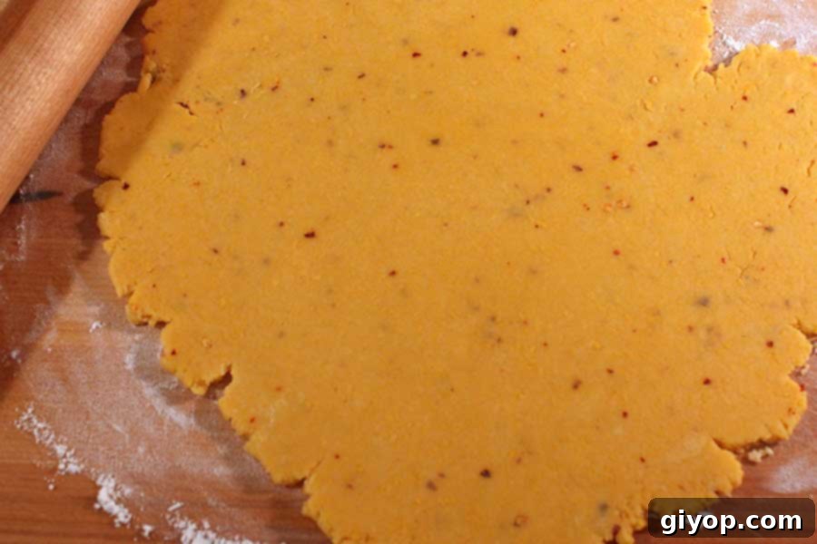 Spicy Cheese Cracker dough rolled out thinly and evenly on a wooden board, ready for cutting. The dough has a uniform color and texture.