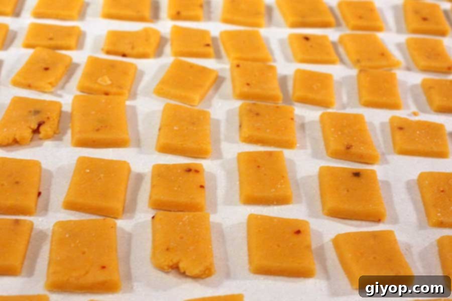 Spicy Cheese Crackers cut into neat squares and arranged on a parchment-lined baking sheet, with small holes poked in each. They are evenly spaced for baking.