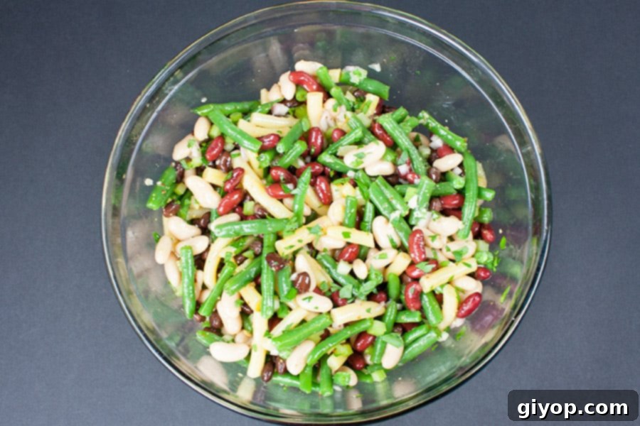 Five Bean Salad ingredients fully tossed with the dressing in a large glass mixing bowl, showcasing the vibrant colors.