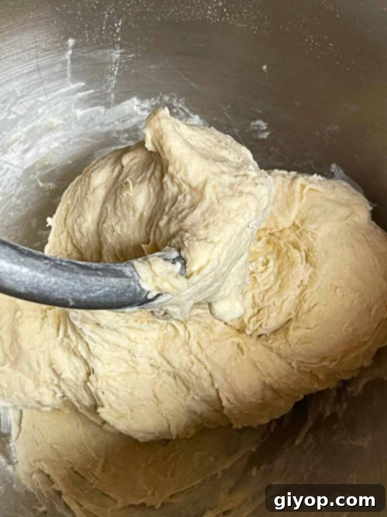 Pizza dough being mixed in a stand mixer bowl.
