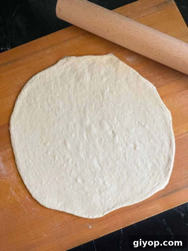 Pizza dough rolled out on a large wooden cutting board.