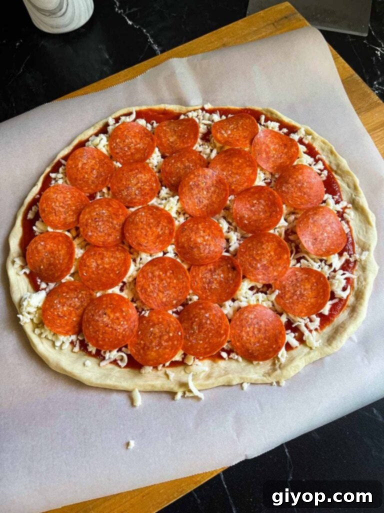 An unbaked pepperoni pizza on parchment paper.