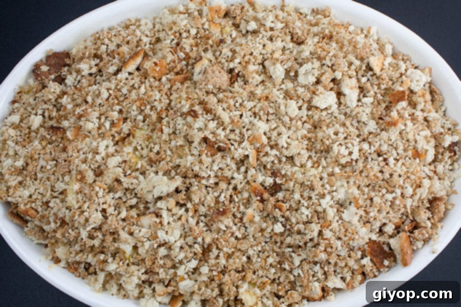 Southern Golden Squash Bake 4 Southern Yellow Squash Casserole in an oval white baking dish, topped with golden-brown bread crumbs, just out of the oven.