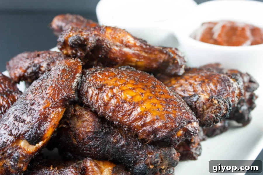 Amazing Smoked Chicken Wings piled high on a white platter with bbq sauce in the background.
