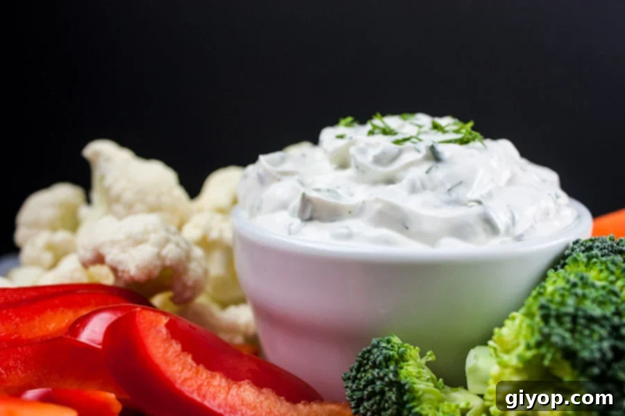 A vibrant Fresh Herb Vegetable Dip in a white bowl, surrounded by an array of colorful fresh vegetables like carrots, celery, bell peppers, and cucumbers, arranged attractively on a platter, ready for dipping.