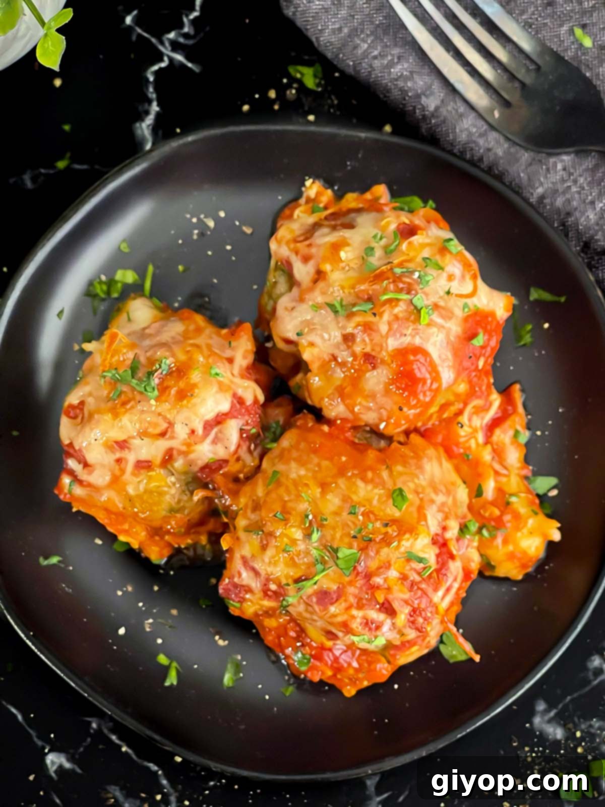 Easy baked parmesan meatballs garnished with chopped Italian flat leaf parsley on a dark plate.