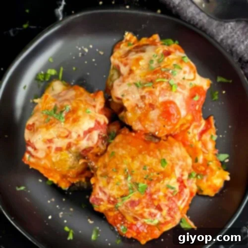 Easy baked parmesan meatballs garnished with chopped Italian flat leaf parsley on a dark plate.