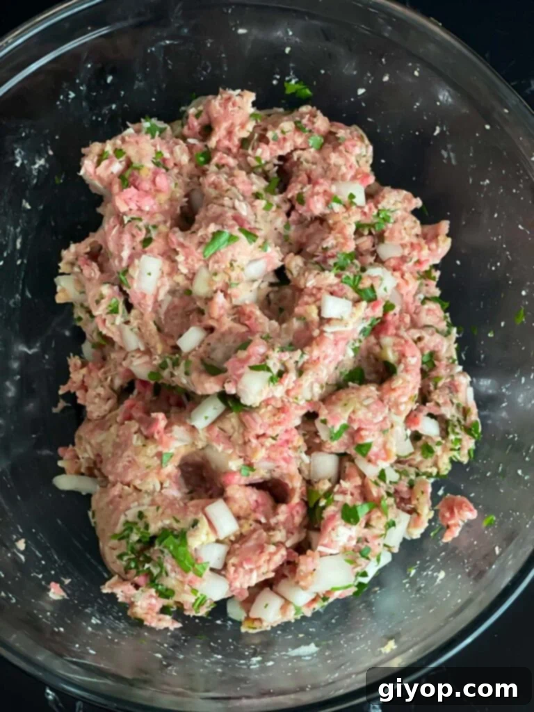 Parmesan meatball mixture in a glass bowl on a dark surface.