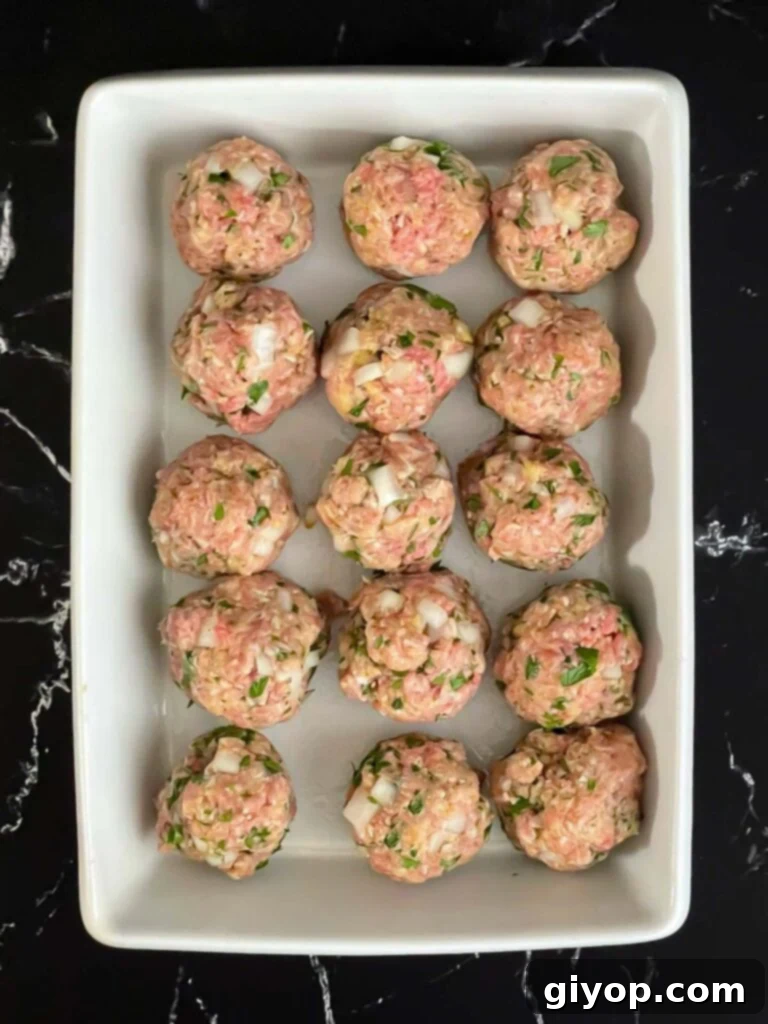 Unbaked parmesan meatballs in a light casserole dish on a dark surface.