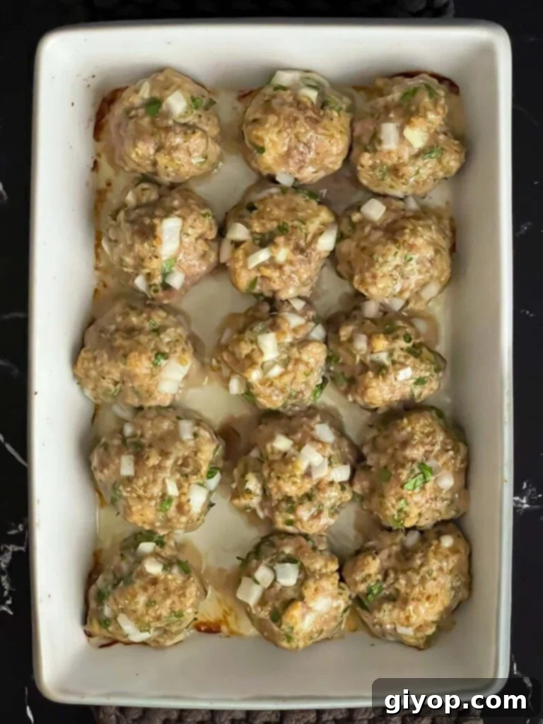 Baked parmesan meatballs out of the oven in a light casserole dish.