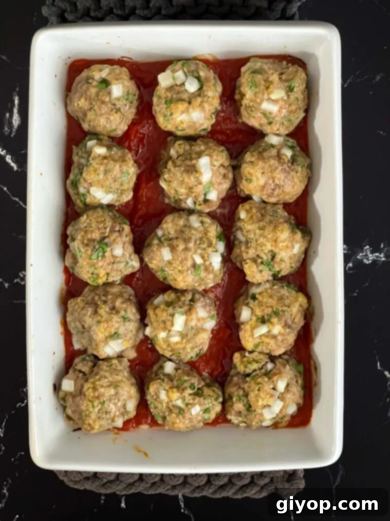 Marinara sauce in the bottom of the casserole dish with the parmesan meatballs placed on top.