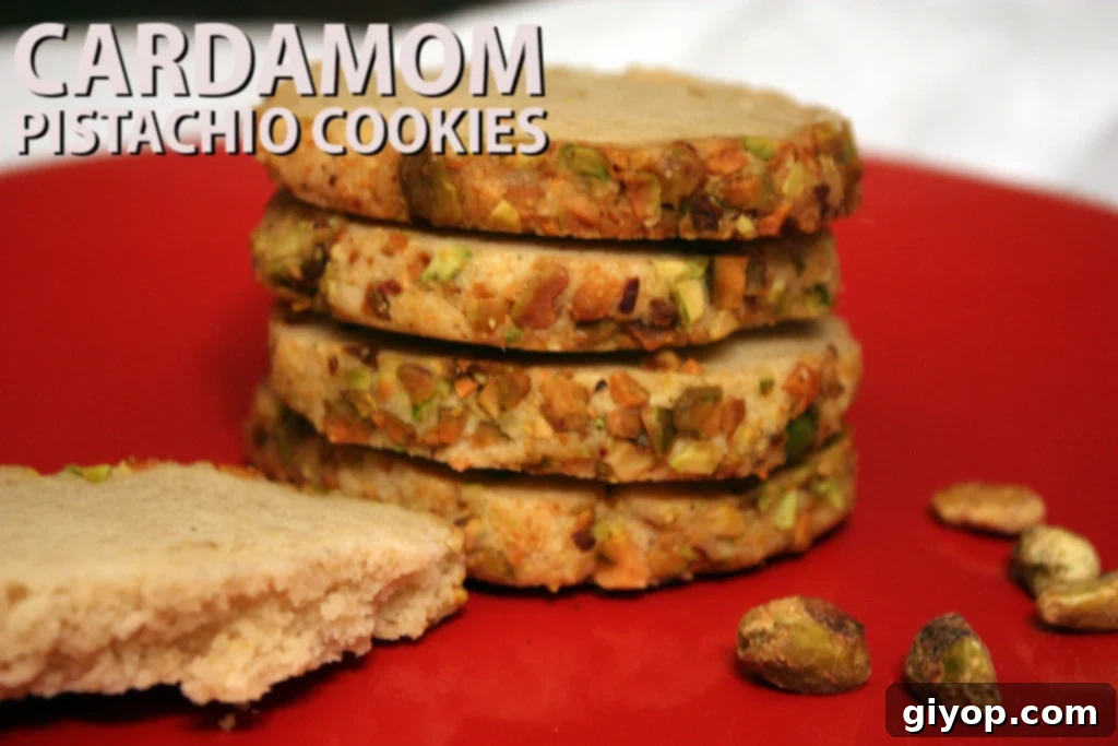 Stacked cardamom pistachio shortbread cookies on a red plate, lightly dusted with powdered sugar and garnished with chopped pistachios.