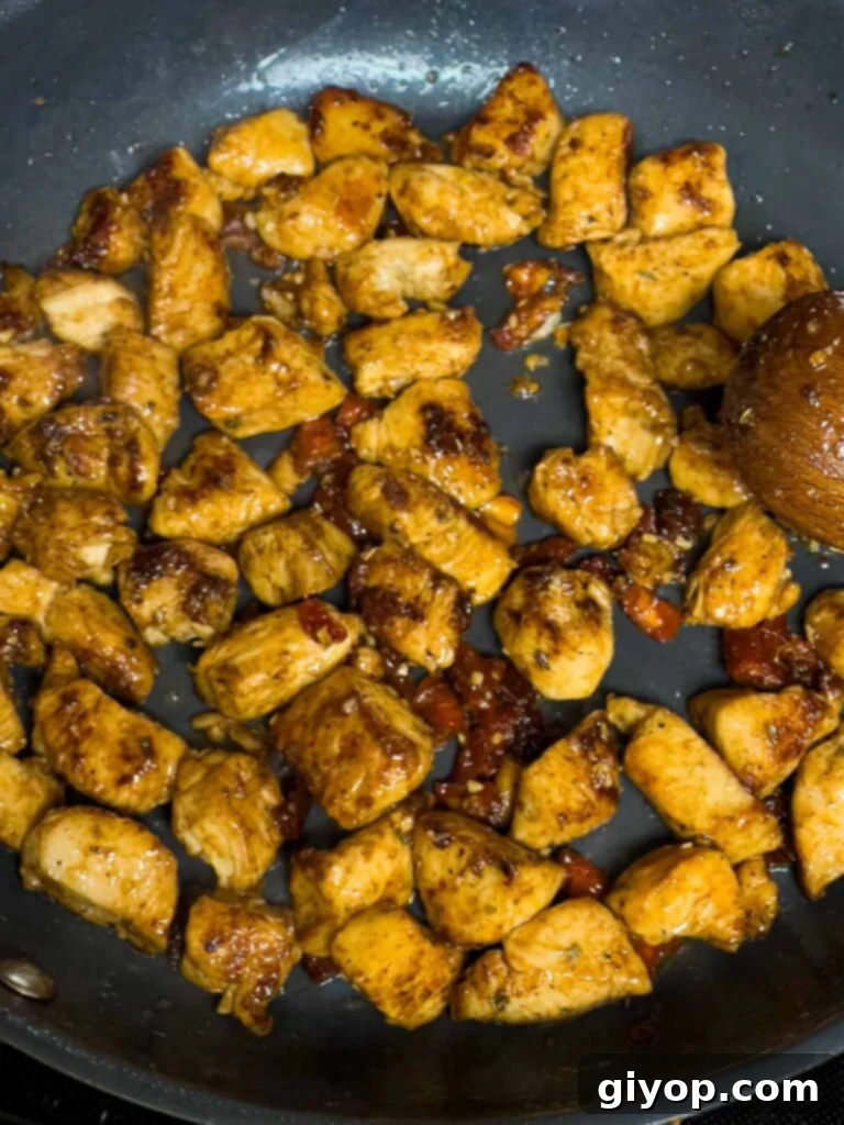 Zesty Louisiana Chicken Pasta 7 Browned chicken breast and sun-dried tomatoes simmering with spices in a skillet, creating a rich aroma.