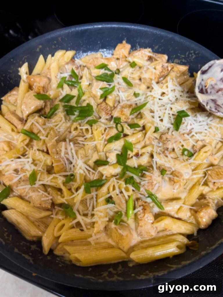 Zesty Louisiana Chicken Pasta 9 Green onions and grated Parmesan cheese being added to Cajun chicken pasta in a skillet and mixed in.