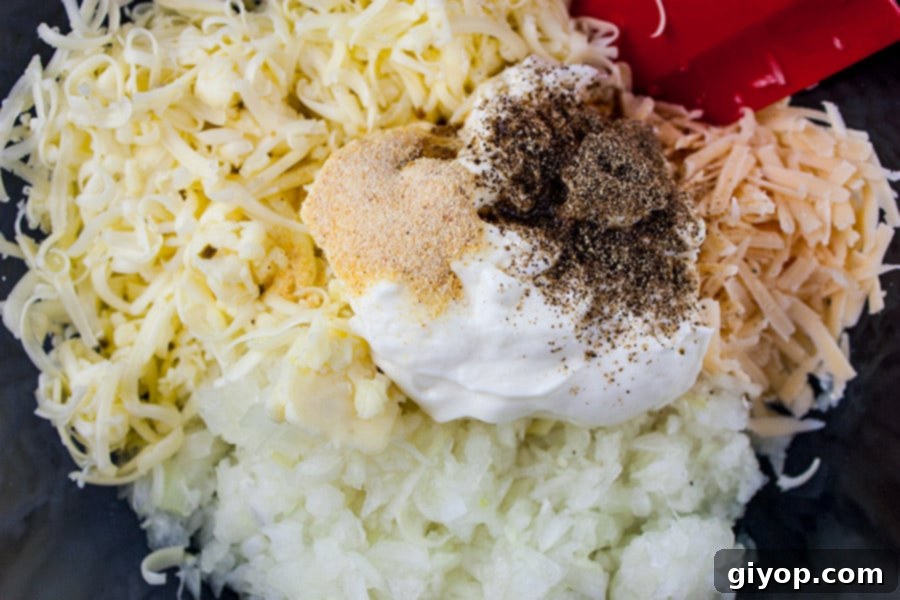 Ingredients for Baked Vidalia Onion Dip in a clear glass bowl, showing finely diced onions and shredded cheeses.