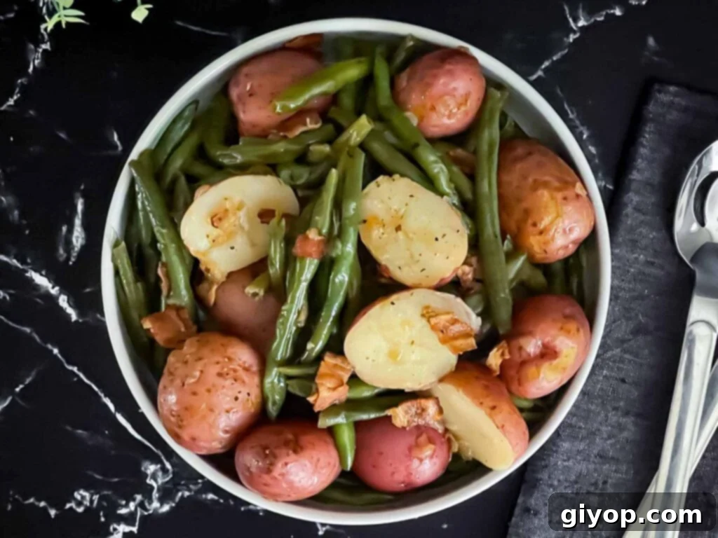 Southern green beans and potatoes in a round light colored bowl on a dark surface.