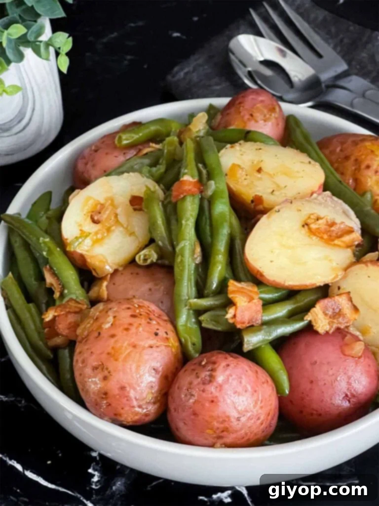 Southern green beans and potatoes in a round light colored bowl on a dark surface.