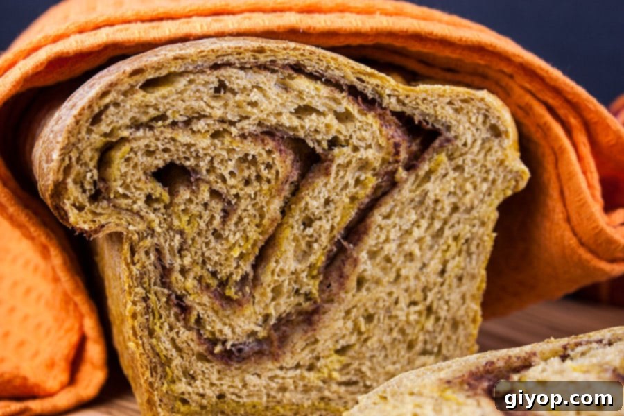 A perfectly sliced loaf of homemade Pumpkin Cinnamon Swirl Bread, beautifully displaying the intricate cinnamon ribbon, draped with an orange linen towel.