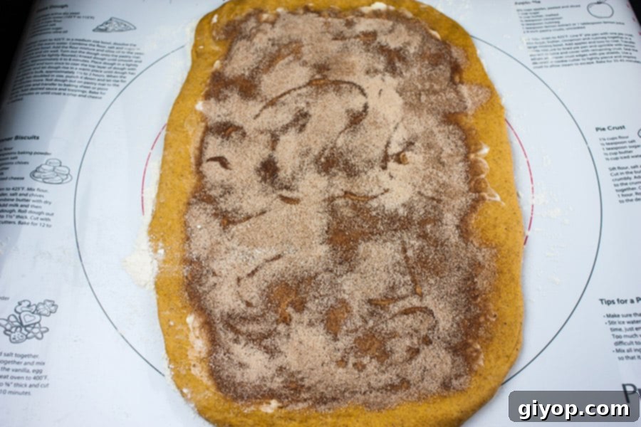The rolled-out pumpkin dough on a pastry mat, generously covered with a spiced cinnamon sugar and softened butter filling, ready to be rolled into a log.