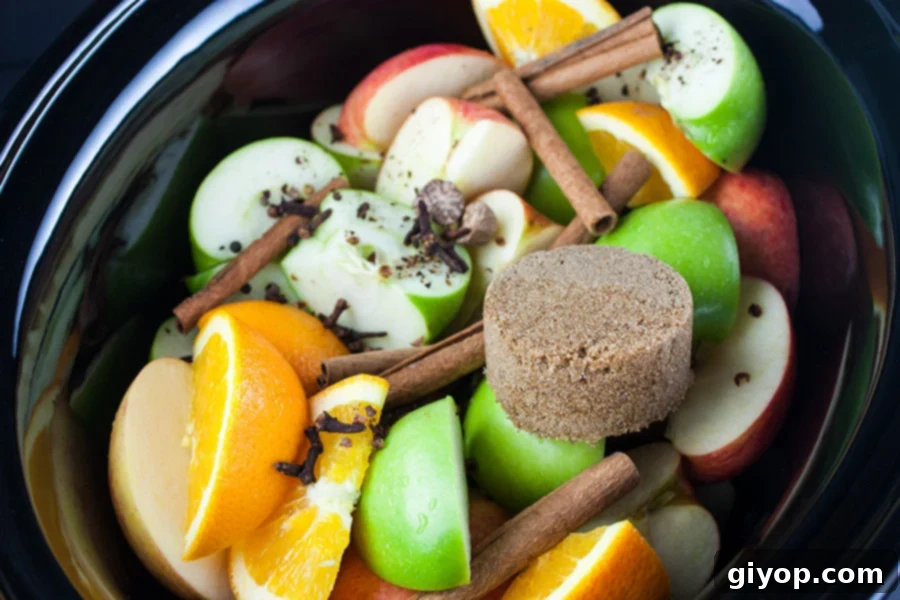 Apples, orange, cinnamon sticks and spices in the crock of a slow cooker.